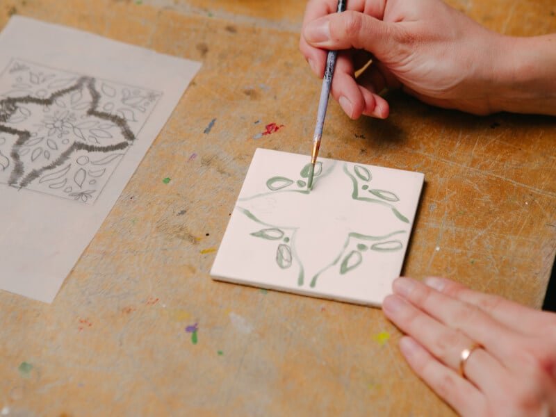 Person painting a ceramic tile
